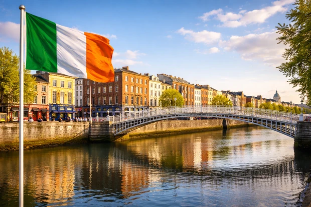 Ha’penny Bridge sul fiume Liffey a Dublino, capitale dell’Irlanda, con bandiera nazionale ed edifici storici