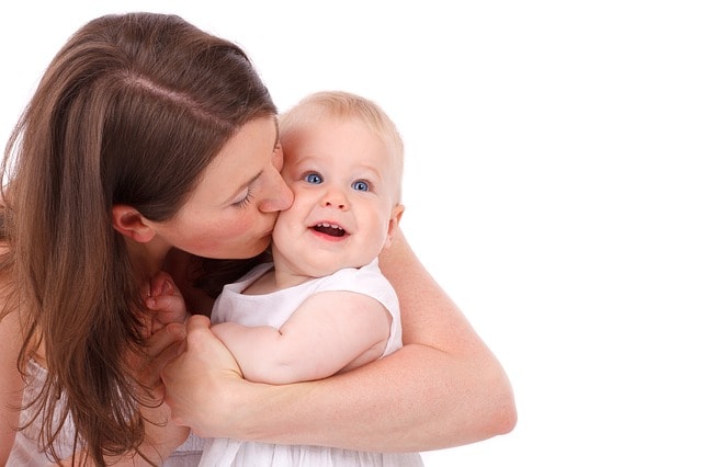 Una madre che bacia la propria figlia sulla guancia. Occhi azzurri.